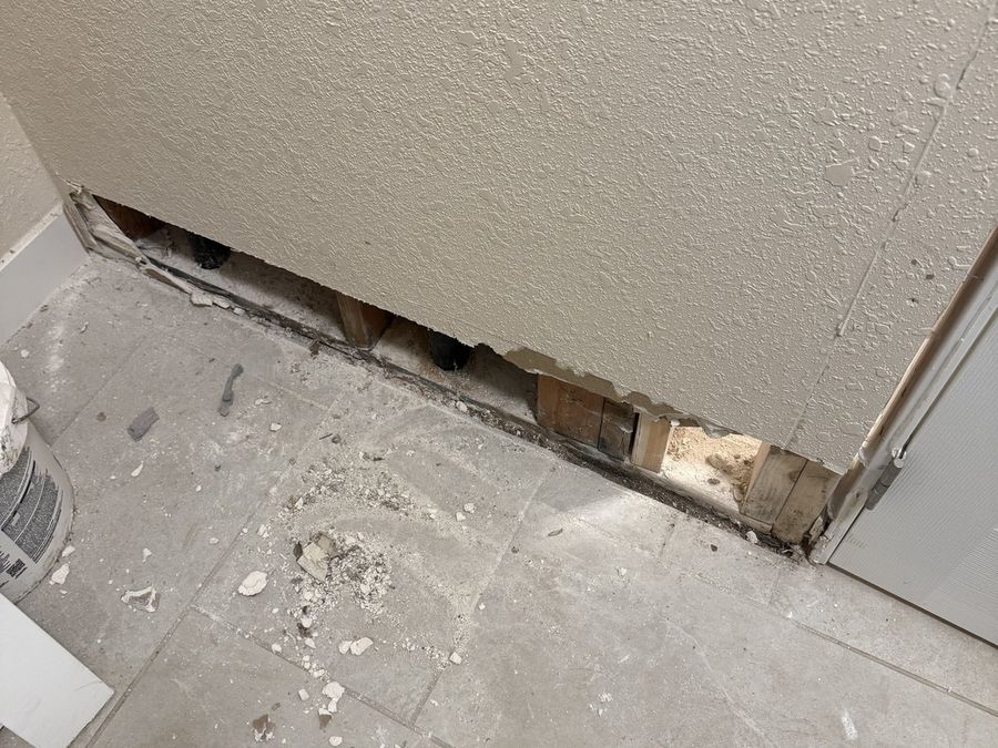 The base of a wall opened to expose wet framing behind a shower