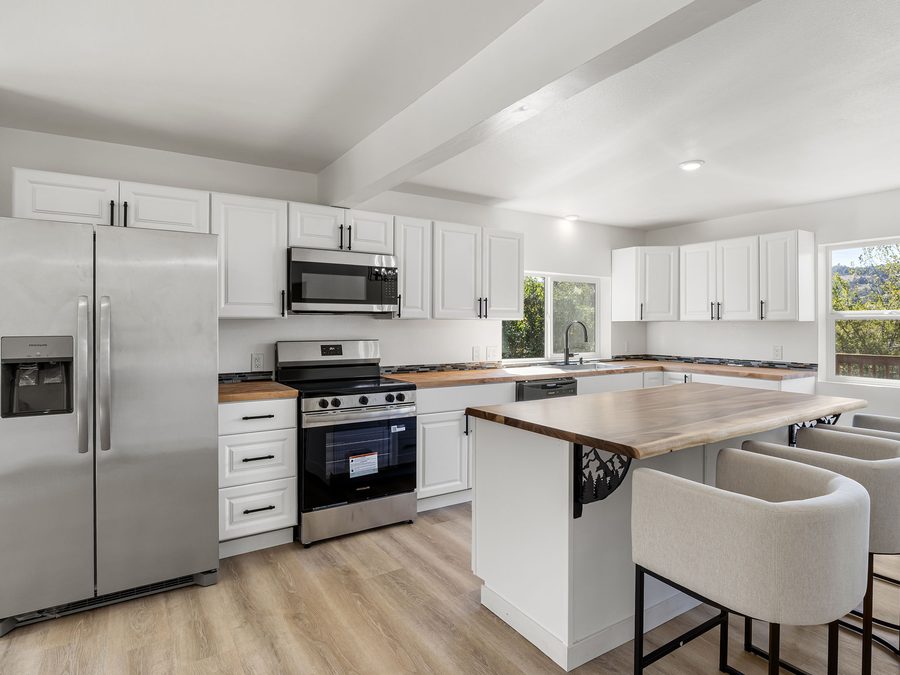 A remodeled kitchen with white cabinets, wood counters, a live-edge island and new flooring